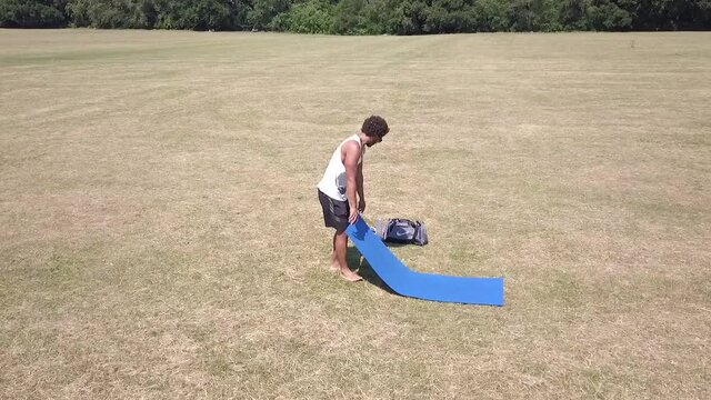 Man laying out a mat in the park to practice yoga on. Full HD. Royalty free. Slow Motion