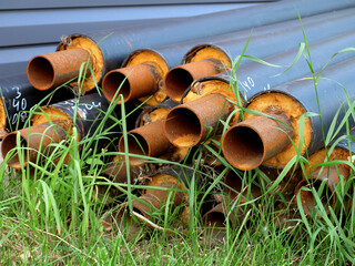 pile of forgotten slightly rusty pipes in thermal insulation, laying in grass