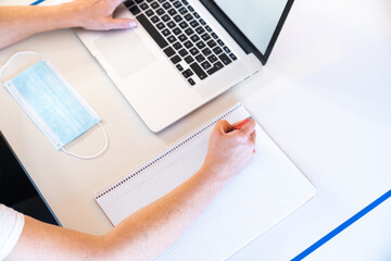 Student doing homework with a notebook and a laptop on a desk with social distancing measures to prevent the spread of the coronavirus.