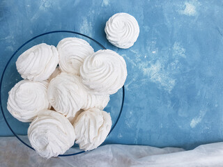 White marshmallows in a bowl on a blue textured background with copy space 
