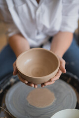 Fototapeta na wymiar The female potter finished making a clay vase remove it from the potter's wheel. Creating vase of white clay. Making ceramic products from white clay, closeup