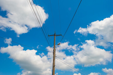 Obraz premium Utility pole and overhead wires and cables in a blue cloudy sky in sunlight in summer