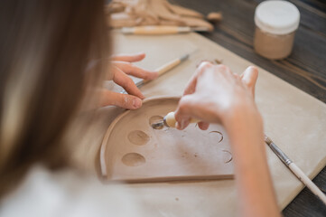 Craftsman hands connect the clay parts made of raw clay, master fingers work with pieces of clay, female sits at a workshop behind the table