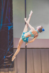 Picture of girl in light blue costume is showing acrobatic ticks on pylon. Straight legs above the...