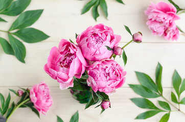 top view on bouquet of fresh pink peony and buds in vase on light wooden background with leaves, postcard