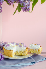 French dessert, whole, slice, with lilac flowers. lemon tartlet with Italian meringue, whipped cream in cut on pink background with copy space, text. creative decoration. vertical