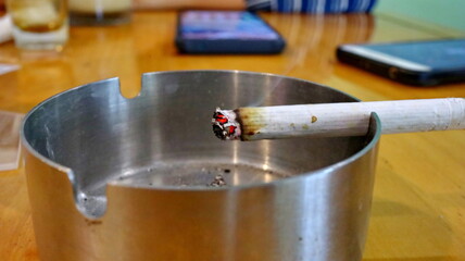 cigarettes burning on an ashtray, with selective focus, image noise and blurry                     ...