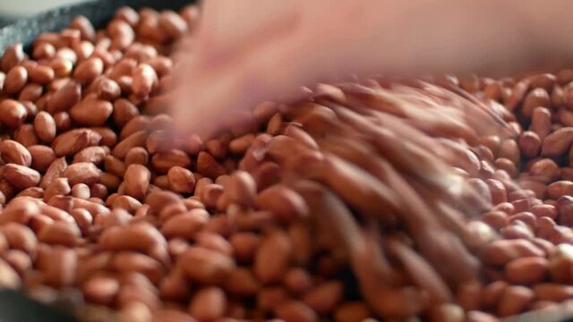 Peanuts groundnuts roasted in a pan and a woman stirs the nuts with her hand. Cooking close-up 