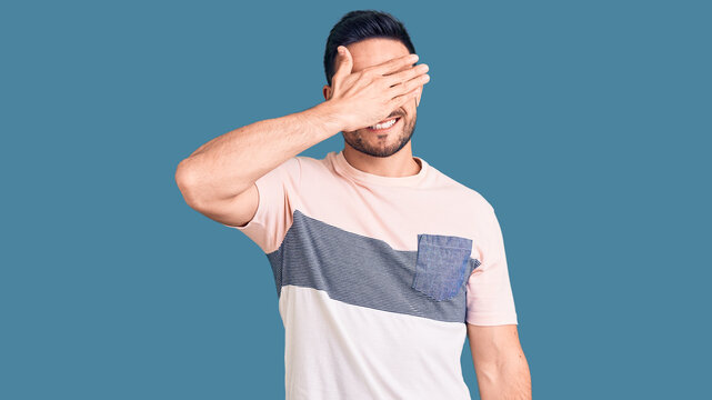 Young handsome man wearing casual clothes smiling and laughing with hand on face covering eyes for surprise. blind concept.