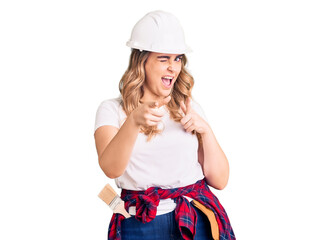 Young caucasian woman wearing security helmet pointing fingers to camera with happy and funny face. good energy and vibes.