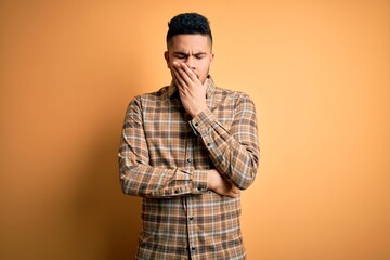 Young handsome man wearing casual shirt standing over isolated yellow background bored yawning tired covering mouth with hand. Restless and sleepiness.