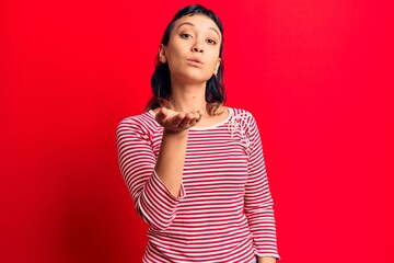 Young woman wearing casual clothes looking at the camera blowing a kiss with hand on air being...