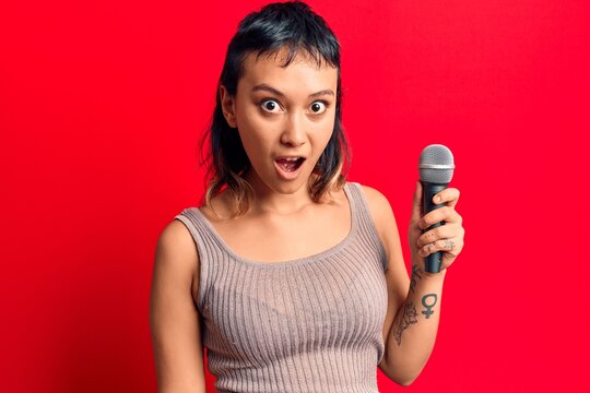Young woman singing song using microphone scared and amazed with open mouth for surprise, disbelief face
