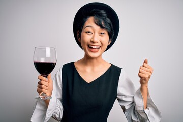 Young beautiful asian sommelier girl drinking glass of red wine over isolated white background screaming proud and celebrating victory and success very excited, cheering emotion