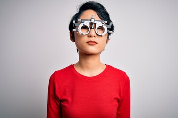 Young beautiful asian girl wearing optometry glasses standing over isolated white background with serious expression on face. Simple and natural looking at the camera.