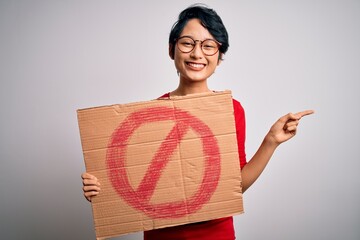 Young beautiful asian girl holding banner with prohibited signal over white background very happy...
