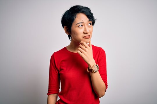 Young beautiful asian girl wearing casual red t-shirt standing over isolated white background Thinking worried about a question, concerned and nervous with hand on chin