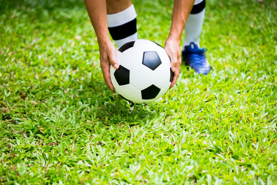 Selective focus to soccer ball with blurry hands of players are putting it on green grass.