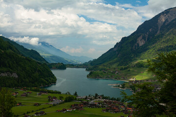 Aerial view of the scenic mountain lake (Lake Lungern) situated in Swiss alps. Lake is surrounded by steep mountains covered with forest as well as a grassland where houses of Lungern is located.