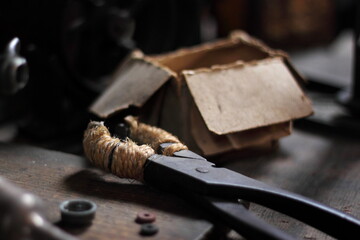 A close up image of a vintage desk in an old workshop. Wooden desk is covered with blacksmith's or plumber's toolkit  including  cast iron pliers, bolts, washers and nuts as well as a box.