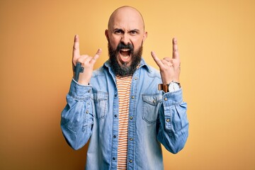 Handsome bald man with beard wearing casual denim jacket and striped t-shirt shouting with crazy...
