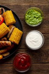 Grilled bbq sausages with vegetables, spices and three sau e on wooden background