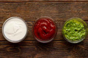 Set of sauces - ketchup, mayonnaise and pesto on wooden background. Top view.