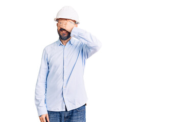 Young handsome man wearing architect hardhat smiling and laughing with hand on face covering eyes for surprise. blind concept.