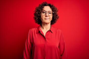 Fototapeta na wymiar Middle age beautiful curly hair woman wearing casual shirt and glasses over red background looking sleepy and tired, exhausted for fatigue and hangover, lazy eyes in the morning.