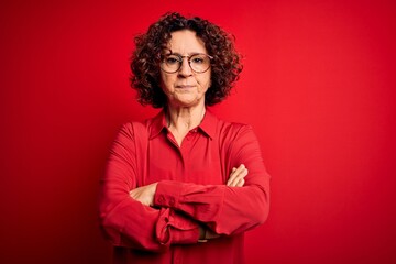Fototapeta na wymiar Middle age beautiful curly hair woman wearing casual shirt and glasses over red background skeptic and nervous, disapproving expression on face with crossed arms. Negative person.