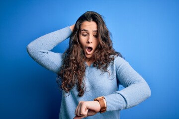 Young beautiful woman with curly hair wearing blue casual sweater over isolated background Looking...