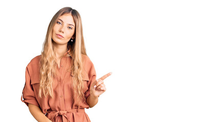 Fototapeta premium Beautiful caucasian woman with blonde hair wearing summer jumpsuit pointing with hand finger to the side showing advertisement, serious and calm face