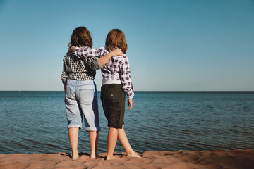 Two girls on the beach looking at the water. View from the back