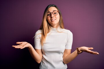 Young beautiful blonde woman with blue eyes wearing casual t-shirt over purple background clueless...
