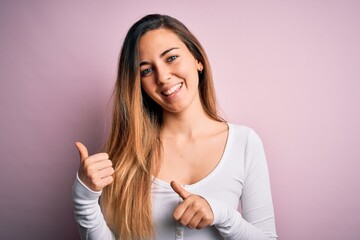 Young beautiful blonde woman with blue eyes wearing white t-shirt over pink background Pointing to the back behind with hand and thumbs up, smiling confident