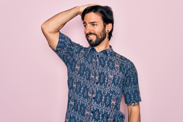 Young handsome hispanic bohemian man wearing hippie style over pink background smiling confident touching hair with hand up gesture, posing attractive and fashionable