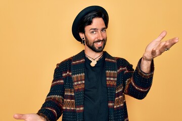 Young handsome hispanic bohemian man wearing hippie style and boho hat smiling cheerful offering hands giving assistance and acceptance.