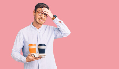 Handsome young man with bear holding takeaway cup of coffee stressed and frustrated with hand on head, surprised and angry face