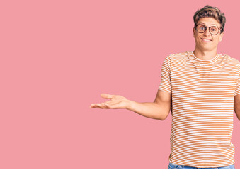 Young handsome man wearing casual clothes and glasses clueless and confused expression with arms...