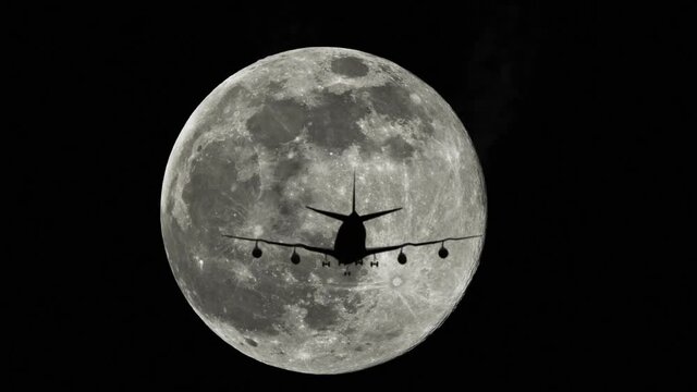 Plane silhouette against a full moon in the sky, airplane flying by the moon