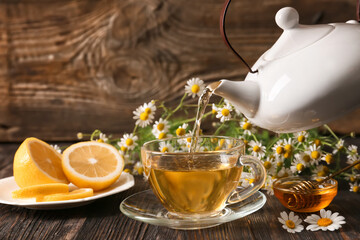 Pouring of chamomile tea from teapot into cup on table