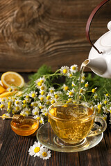 Pouring of chamomile tea from teapot into cup on table