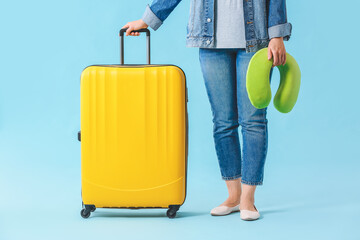 Woman with packed suitcase and travel pillow on color background