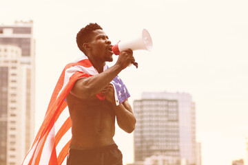 African-American man with the USA flag shouts in a megaphone and protests against the background of...