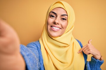 Young beautiful brunette arab woman wearing islamic hijab make selfie by camera with surprise face...