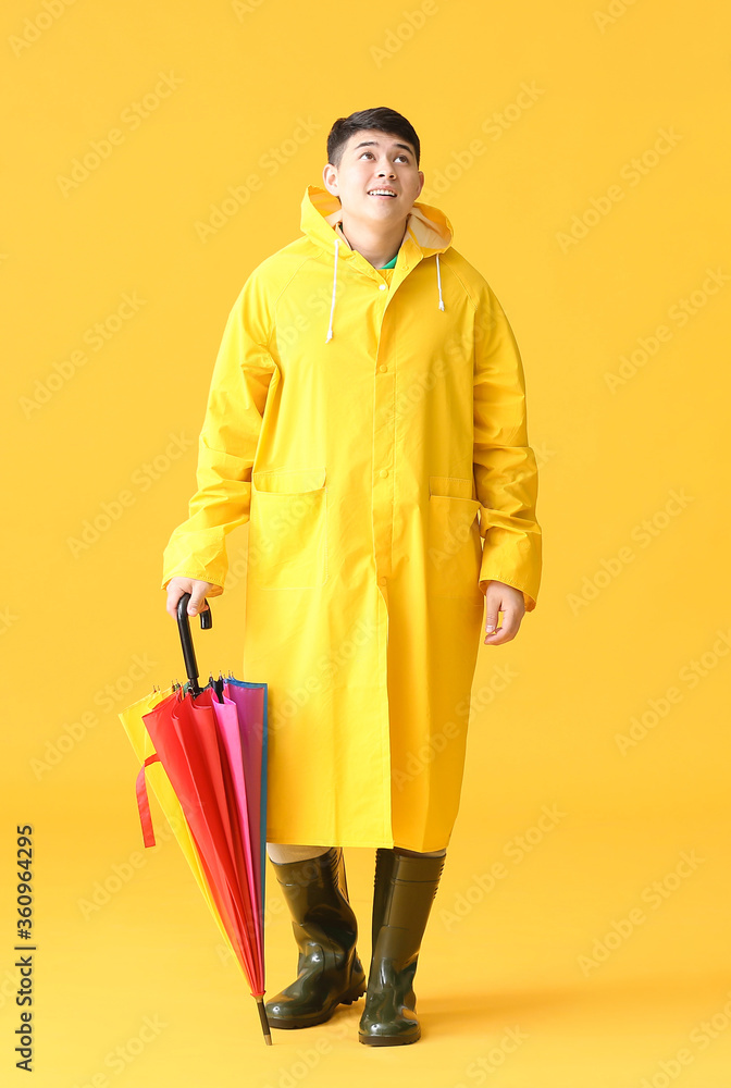 Wall mural young asian man in raincoat and with umbrella on color background