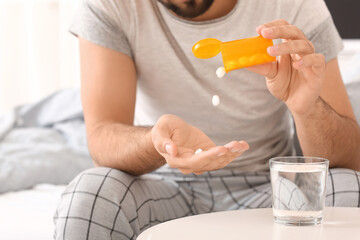 Young man taking sleeping pills in bedroom