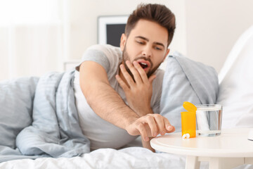 Man taking sleeping pills from table in bedroom