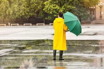 Young Asian man in raincoat and with umbrella on city street