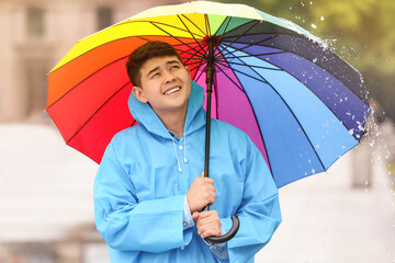 Young Asian man in raincoat and with umbrella on city street